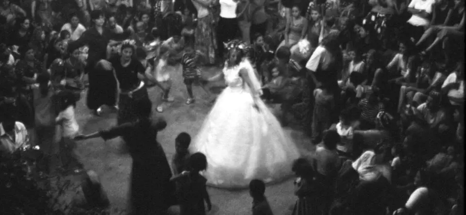 The black and white photo is taken from above and shows a crowd of people dancing, with a dancing bride in a white wedding dress in the middle of the crowd.