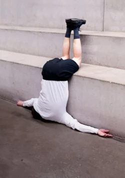 A person is lying upside down on steps made of gray concrete. The person is wearing a white long-sleeved top, short black trousers, black shoes and black stockings. The person's head is not visible.